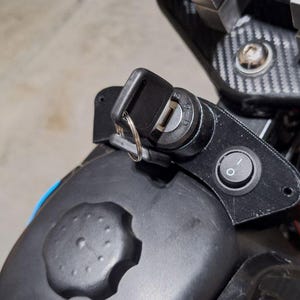 Może przedstawiać: Zbliżenie czarnego włącznika zapłonu z włożonym kluczem, przyciskiem zasilania i czarnym plastikowym elementem. Klucz jest na pierścieniu. Tło jest rozmyte.