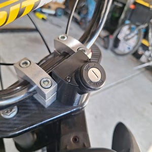May include: Close-up of a motorcycle handlebar assembly. The handlebars are chrome, with a black ignition switch that reads "OFF" and "IGNITION". The assembly includes silver-colored mounting brackets and a black base.
