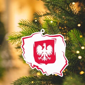 May include: A white Christmas ornament shaped like the outline of Poland with a red shield featuring a white eagle in the center.