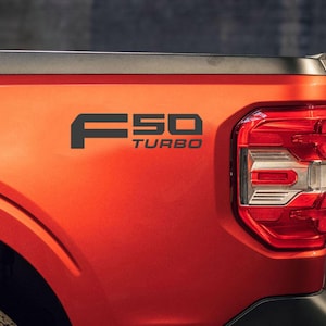 May include: Close-up of a red truck bed with a black "F50 TURBO" emblem. The truck's taillight is visible on the right side. The vehicle's paint has a metallic finish.