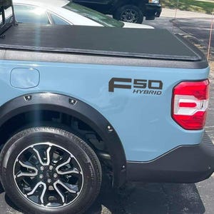 May include: Light blue pickup truck with black accents, a black tonneau cover, and a black wheel. The truck has the text "F50 HYBRID" in black on the side. The taillight is red and white.