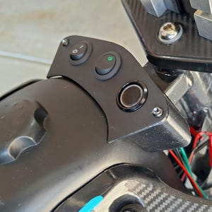 May include: Close-up of a black control panel with three buttons and a power button. The panel is mounted on a black, curved surface. Wires in red and green are visible.