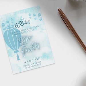 Op de afbeelding: Een blauwe en witte uitnodigingskaart met een decoratief lantaarnontwerp. De tekst luidt "Van onze familie aan de jouwe, je bent uitgenodigd voor een Iftar-feest" en bevat de datum "4 | 16 | 2022", het adres "123 Wet N Wild Way, Arlington TX, 76018".
