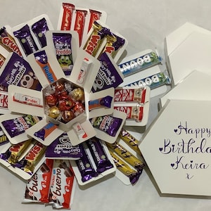 May include: A white hexagonal gift box filled with chocolate bars and sweets. The box is decorated with the text "Happy Birthday Keira". Chocolate brands include Dairy Milk, Kit Kat, and Kinder.