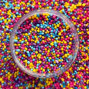 May include: A clear glass jar filled with colorful sprinkles. The sprinkles are a mix of pink, yellow, blue, and purple.