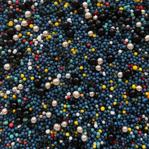 Könnte beinhalten: Nahaufnahme einer Vielzahl von bunten Streuseln, darunter blau, schwarz, gelb, rot, weiß und grün. Die Streusel sind klein und rund und über die Oberfläche verteilt.