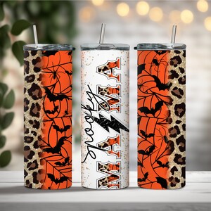 May include: Three stainless steel tumblers with different Halloween-themed designs. The first tumbler has a leopard print and orange pumpkin design. The second tumbler has a white background with the words "Spooky" and "Autumn" in black and gold glitter. The third tumbler has a spiderweb and bat design with orange and black colors.