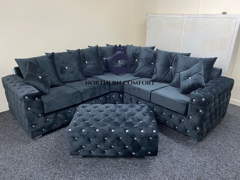 May include: A dark gray sectional sofa and matching ottoman set. The sofa features a tufted design with crystal-like accents and plush cushions. The ottoman mirrors the sofa's design, creating a cohesive living room furniture set.