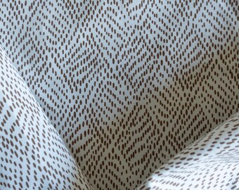 May include: Close-up of a fabric with a repeating pattern of brown, oval-shaped dots arranged in a chevron design on a light blue background. The fabric is folded, showing the texture and pattern.