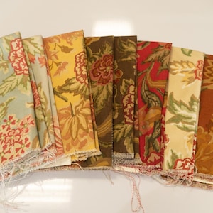 Puede incluir: Una colección de muestras de tela en varios colores, incluyendo azul claro, amarillo, marrón y rojo. Cada muestra presenta un patrón floral con hojas y flores detalladas. Las telas están dispuestas en forma de abanico, mostrando los diferentes diseños.