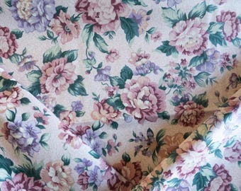 May include: Floral fabric with a repeating pattern of large, detailed flowers in shades of pink, purple, and cream. The leaves are a deep teal green. The fabric is folded, showing the pattern's continuity.