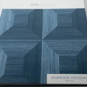 May include: A sample book page titled MORE TEXTURES by SEABROOK DESIGNS SINCE 1910, featuring a blue wallpaper pattern with a geometric design of interlocking cubes and a subtle horizontal wood grain texture throughout the blue surfaces.