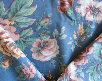 May include: Close-up of blue floral fabric with large pink, cream, and burgundy flowers and green leaves. The fabric is folded, revealing the pattern and texture. The floral pattern is repeated across the fabric.