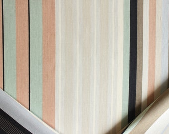 Puede incluir: Un primer plano de una tela a rayas con colores alternos de beige, marrón claro, verde claro y melocotón. La tela está doblada por la mitad, mostrando el patrón en ambos lados.