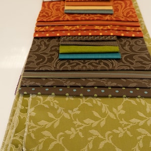 Może przedstawiać: Kolekcja próbek tkanin w różnych wzorach i kolorach. Próbki obejmują wzory kwiatowe, w kropki i wzorzyste w odcieniach pomarańczowego, brązowego, zielonego i niebieskiego. Tkaniny są ułożone warstwowo.