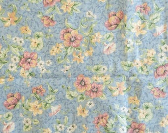 May include: A light blue floral fabric with a repeating pattern of pink, yellow, and white flowers. The flowers are interspersed with green leaves and vines, creating a delicate and feminine design. The fabric has a slightly textured appearance.