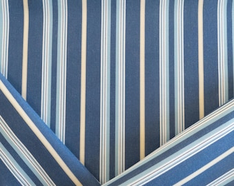 May include: Close-up of blue fabric with vertical stripes in white, light blue, and beige. The fabric is folded in two places, creating a triangular shape on the left and right sides, revealing the striped pattern.