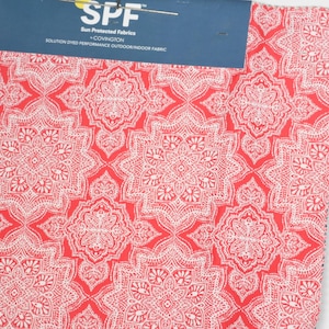 May include: A fabric swatch featuring a repeating white mandala-style pattern on a vibrant red background. The top header is dark blue with white text reading SPF Sun Protected Fabrics by COVINGTON SOLUTION DYED PERFORMANCE OUTDOOR/INDOOR FABRIC.