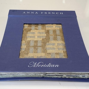 May include: A blue fabric swatch book with the text "Anna French" and "Meridian" on the cover. The fabric swatch is a woven, beige and gold pattern.