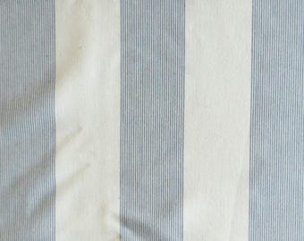 May include: Close-up of a fabric with vertical stripes. Alternating stripes of light blue and white create a simple, classic pattern. The fabric appears to be cotton or a similar material, with a slightly textured surface.