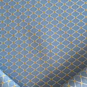 May include: Light blue fabric with a repeating pattern of white diamond shapes and small yellow dots at the intersections. The fabric is folded over in the lower left and right corners, showing the texture.