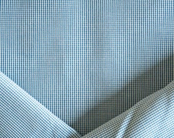May include: Close-up of a blue and white striped fabric. The fabric is folded, creating diagonal lines and shadows. The pattern is a classic, vertical stripe design, suitable for clothing or home decor.