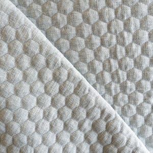 May include: A close-up of a grey quilted fabric with a hexagonal pattern. The fabric has a soft, textured surface.