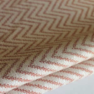 May include: Close-up of a folded fabric with a pink and white chevron pattern. The fabric has a textured surface and a subtle sheen.