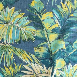 May include: A fabric with a tropical leaf pattern. The design features large, stylized leaves in shades of teal, yellow, and cream against a dark blue background. The leaves have a watercolor effect.