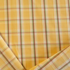 May include: Close-up of yellow plaid fabric with red and green stripes. The fabric is folded over, revealing the pattern and texture. The plaid design is a classic pattern, suitable for various sewing projects.
