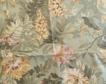 May include: Floral fabric featuring a repeating pattern of large, stylised flowers in peach, cream, and yellow against a muted green backdrop. The fabric has a textured appearance, with visible weave details.