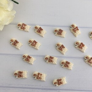 May include: A collection of 15 white sleeping lamb charms with brown bows. The charms are made of polymer clay and are perfect for adding a touch of whimsy to crafts and projects.