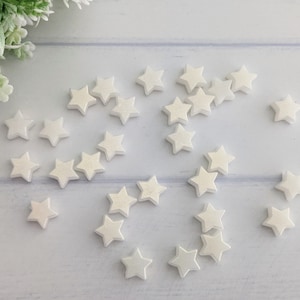 May include: A collection of white pearl-like star-shaped embellishments scattered on a light blue surface.
