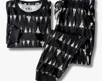 Puede incluir: Un conjunto de pijama negro de manga larga con un patrón de árboles de Navidad blancos y pequeños detalles de estrellas. El conjunto incluye una camiseta de cuello redondo con puños acanalados y pantalones con cintura elástica.