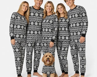 May include: Matching black and white long-sleeve pajama sets featuring a repeating snowflake and geometric pattern. The set includes crew neck tops and full-length pants with ribbed cuffs, worn by four adults and one dog in a matching shirt.