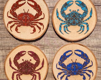May include: Four round wooden coasters with a decorative crab design. Two coasters feature a blue crab with intricate details, and two coasters feature a red crab with intricate details.
