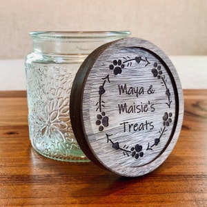 May include: A wooden lid with a floral design and the text "Maya & Maisie's Treats" engraved on it. The lid is for a glass jar with a textured floral design.