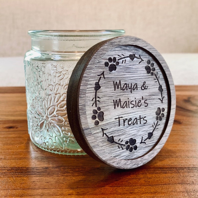 May include: A wooden lid with a floral design and the text "Maya & Maisie's Treats" engraved on it. The lid is for a glass jar with a textured floral design.