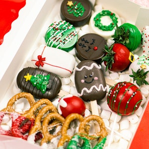 May include: A festive box filled with Christmas-themed treats. Includes chocolate-covered Oreos decorated with Christmas trees and wreaths, chocolate-covered strawberries, and pretzels dipped in red and green chocolate. The box is lined with marshmallows.