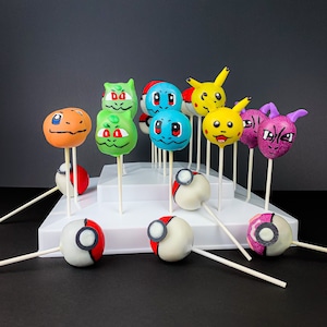 May include: A tiered cake stand holds a variety of colorful Pokemon character cake pops. The cake pops are decorated with different Pokemon characters, including Pikachu, Bulbasaur, Charmander, Squirtle, and more. The cake pops are on white sticks and are arranged in a circle on the stand.