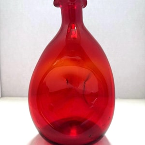 May include: A vibrant red glass vase with a rounded, bulbous body and a narrow neck. The top of the vase features a distinct, ruffled, or crimped rim design. The glass is translucent, allowing light to pass through the deep red color.