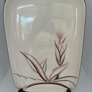 May include: A rectangular off-white ceramic serving platter with rounded corners and a dark brown rim. The centre features a stylised botanical illustration of a thistle-like plant with soft pink and brown brushstroke details on the surface.