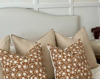 May include: Two brown and white floral patterned throw pillows on a white bed with a white headboard. The pillows are on top of a white and brown patterned bedspread.