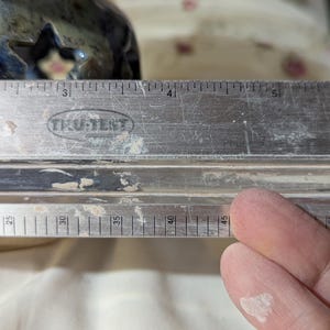 K&ouml;nnte beinhalten: Ein Metalllineal mit der Marke "TRU-TEST" ist abgebildet. Das Lineal ist mit Zentimetern markiert. Das Bild zeigt auch einen Teil eines blau-gr&uuml;nen Keramikobjekts. Das Lineal misst etwa 11,4 cm.