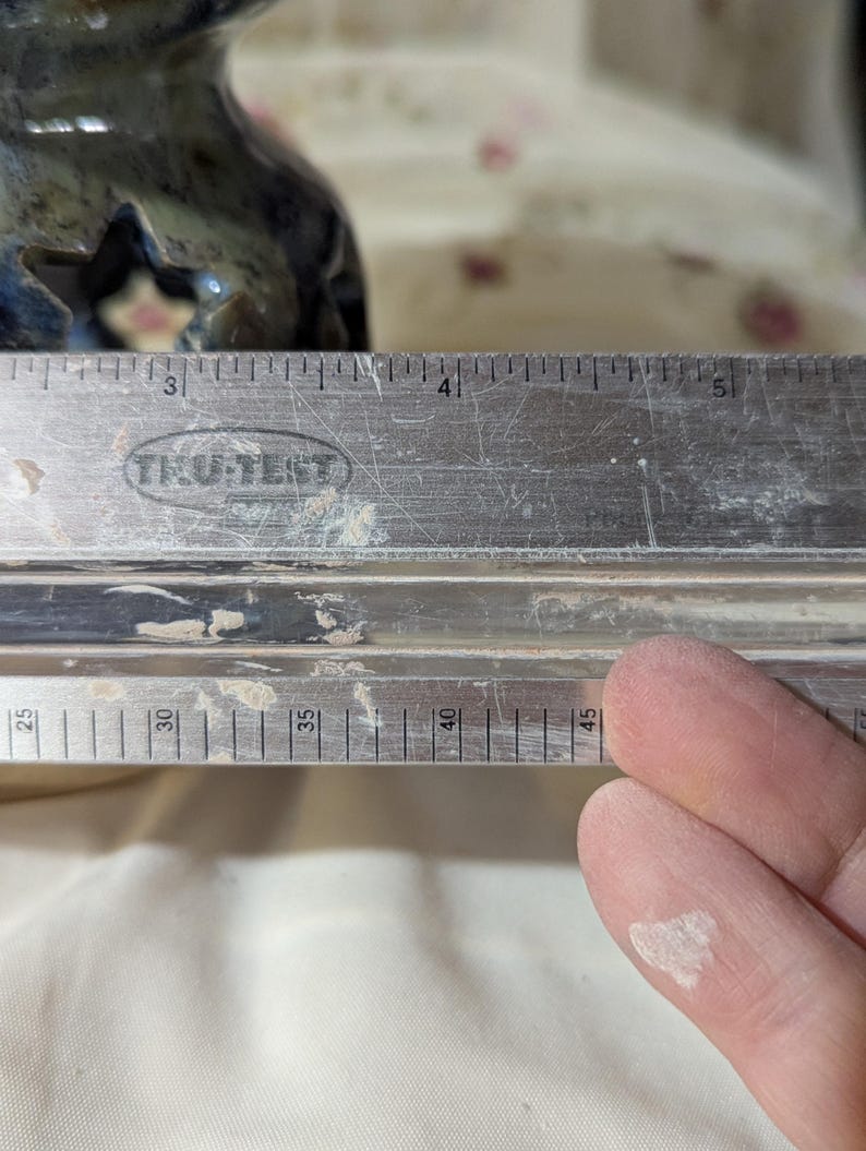K&ouml;nnte beinhalten: Ein Metalllineal mit der Marke "TRU-TEST" ist abgebildet. Das Lineal ist mit Zentimetern markiert. Das Bild zeigt auch einen Teil eines blau-gr&uuml;nen Keramikobjekts. Das Lineal misst etwa 11,4 cm.