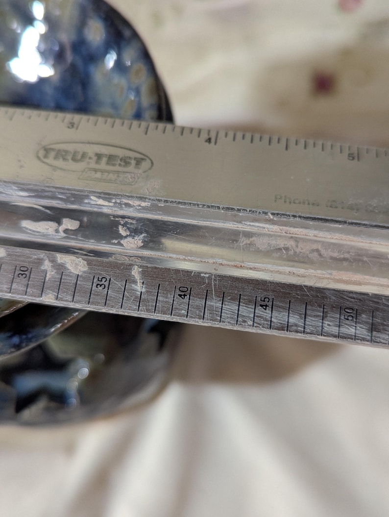 K&ouml;nnte beinhalten: Ein Edelstahl-Lineal mit dem Text "TRU-TEST" liegt &uuml;ber einer Keramikschale. Das Lineal zeigt Messungen in Zentimetern, von 76 cm bis 127 cm. Die Schale hat eine blaue und braune Glasur.
