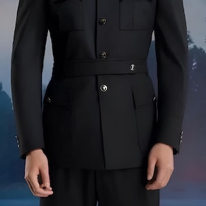 Op de afbeelding: Een zwart colbert met een mandarijnkraag, vier voorzakken en een riem. Het colbert heeft een knoopsluiting en is gemaakt van een gladde stof.