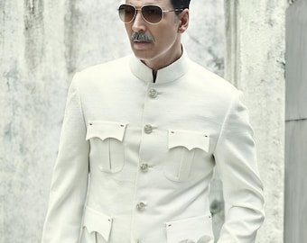 Pode incluir: Um blazer branco com gola mandarim e vários bolsos. O blazer tem fecho de botões e é feito de um tecido texturizado.