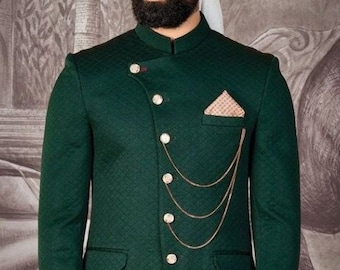 Puede incluir: Una chaqueta verde oscuro con un detalle de cadena dorada y un pañuelo de bolsillo. La chaqueta tiene un cuello mandarín y un cierre de botón único. El hombre lleva pantalones beige y zapatos marrones.
