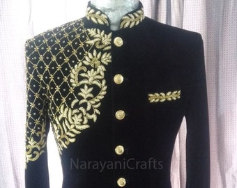 Puede incluir: Una chaqueta de terciopelo negro con bordados dorados. La chaqueta tiene un cuello mandarín y botones dorados. El bordado presenta un diseño floral y un patrón geométrico. El texto "NarayaniCrafts" es visible en la chaqueta.